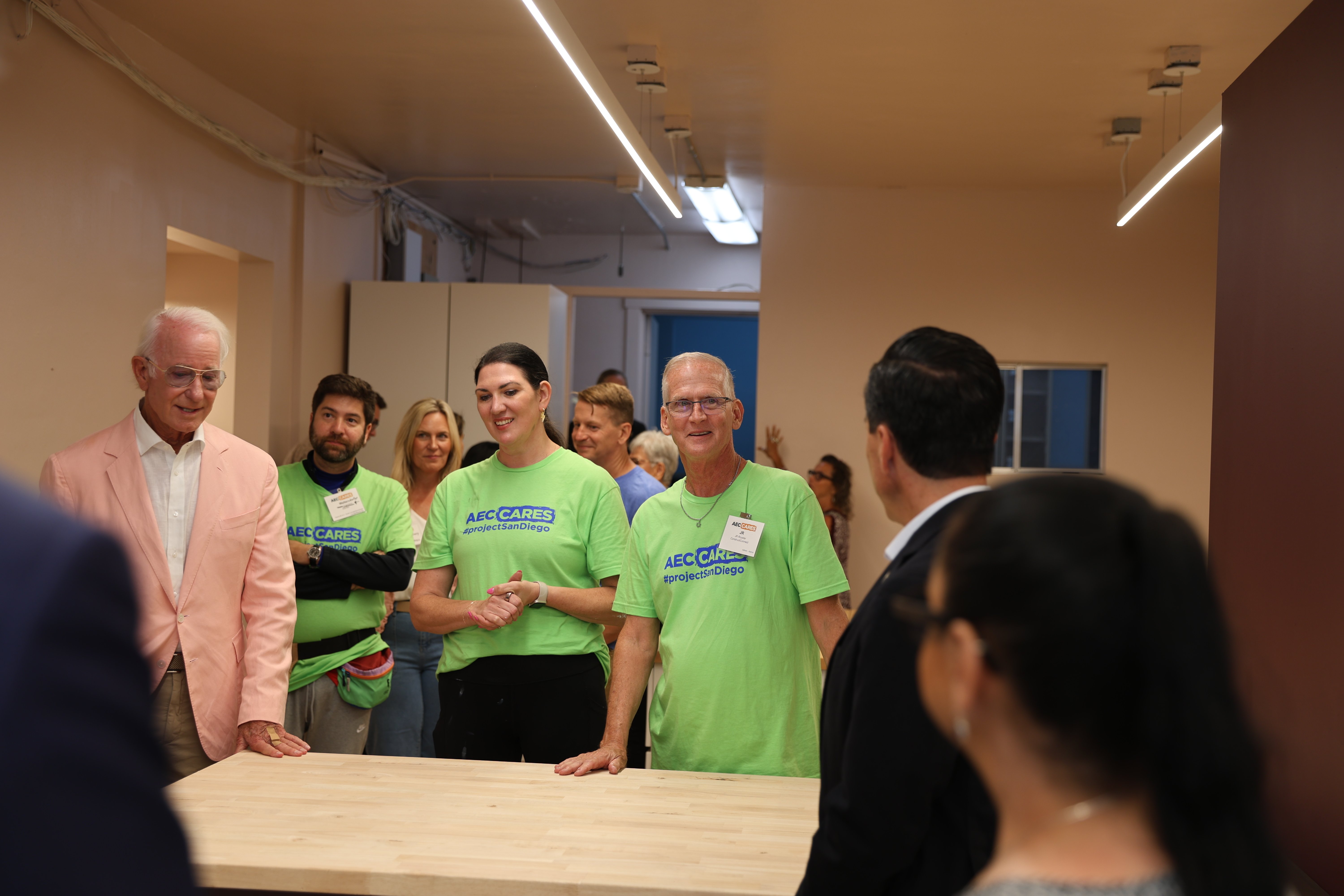 AEC Cares volunteers and guests gather indoors around a table during a Project San Diego event. 