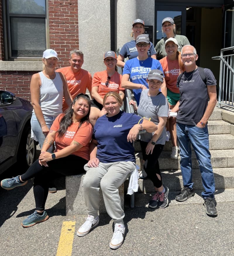 The AEC Cares Steering Committee smiling outside a brick building on a sunny day.