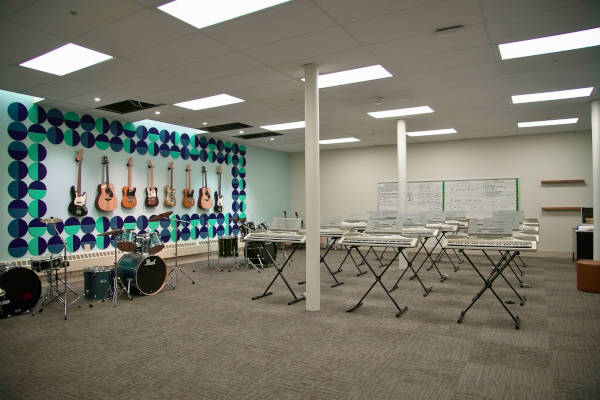 Music classroom with guitars on the wall, a drum set, rows of keyboards, and whiteboards on the wall.