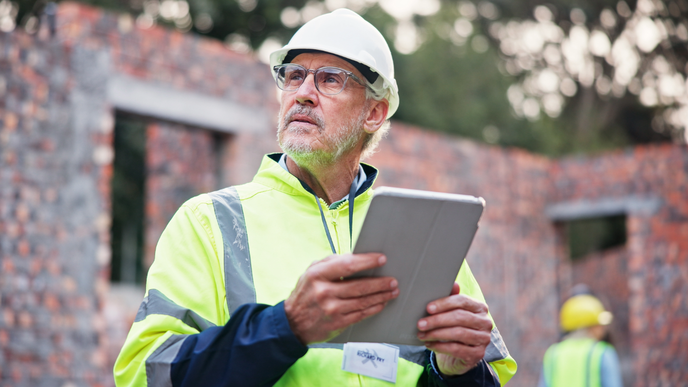 Construction worker wearing a yellow jack and hardhat with a tablet in hand