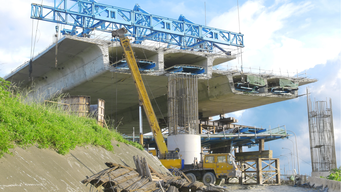 Concrete bridge under construction with cranes, showing multiple spans supported by columns and temporary formwork at an active infrastructure job site.