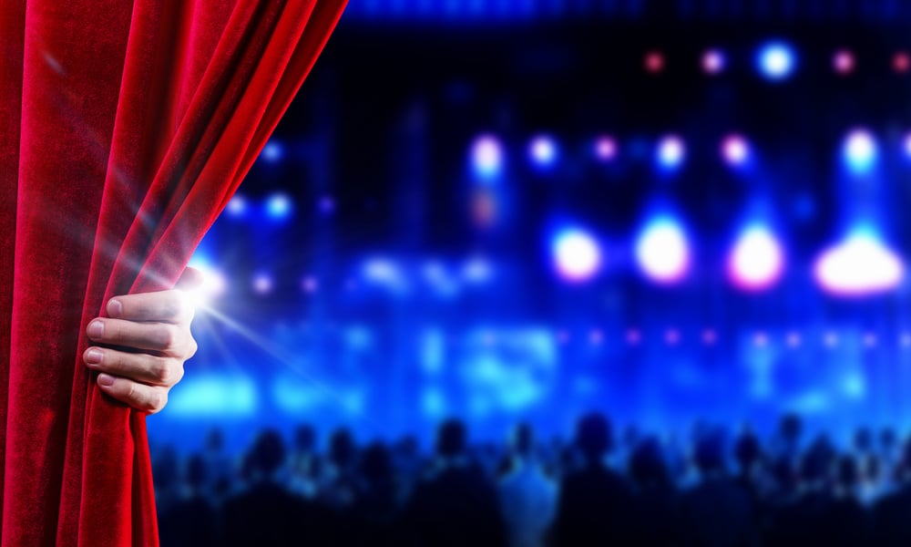 a business person pulls back the velvet red curtain at a concert venue