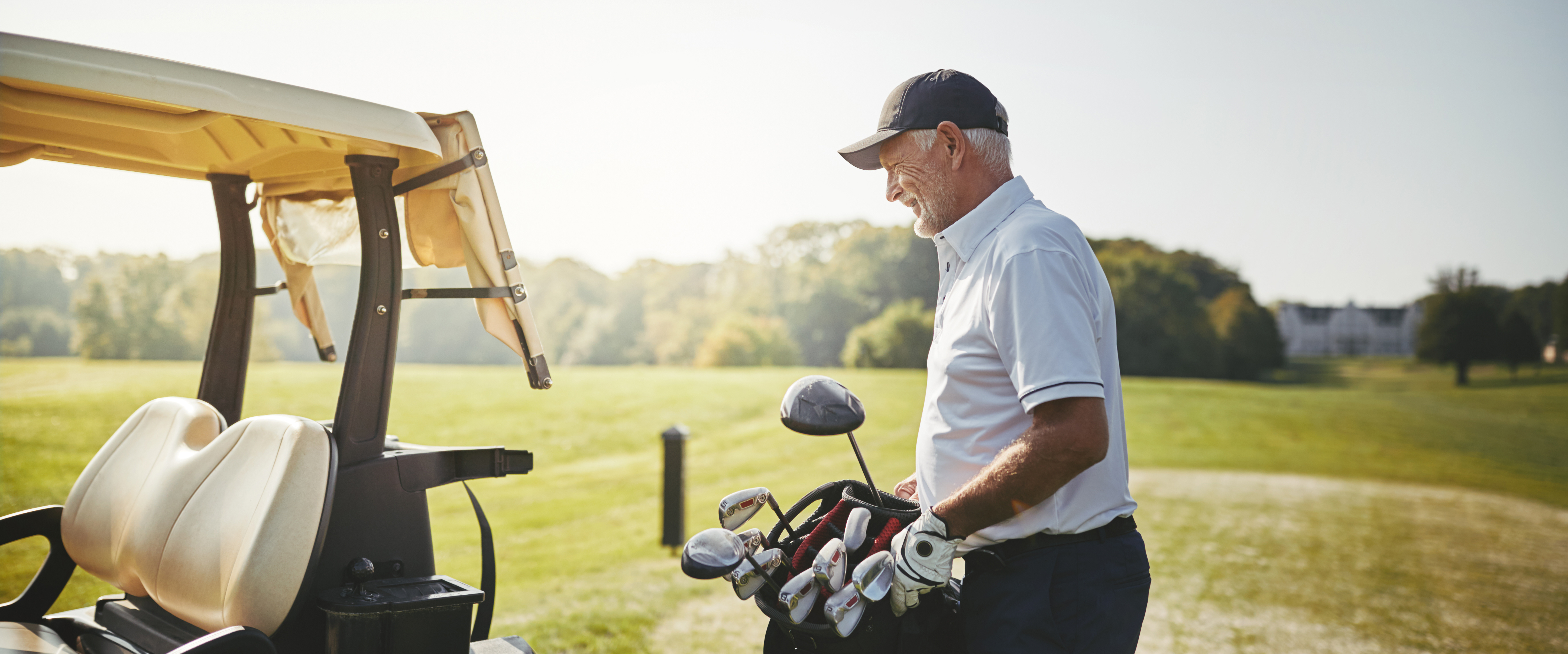Elderly man on a golf course carrying a bag full of golf clubs