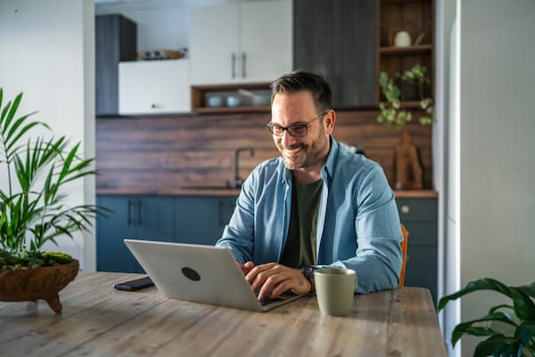 Man smiling while working on a laptop sitting at a table.